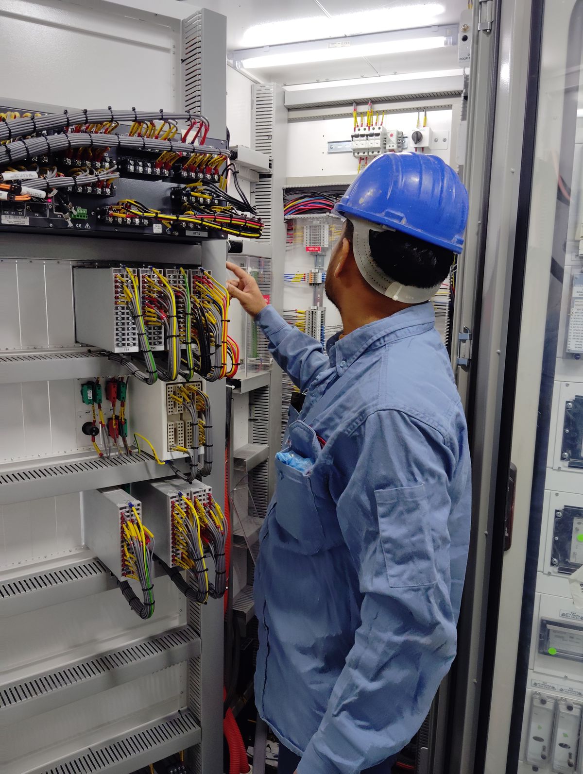 Eletricista revisando quadro elétrico industrial.