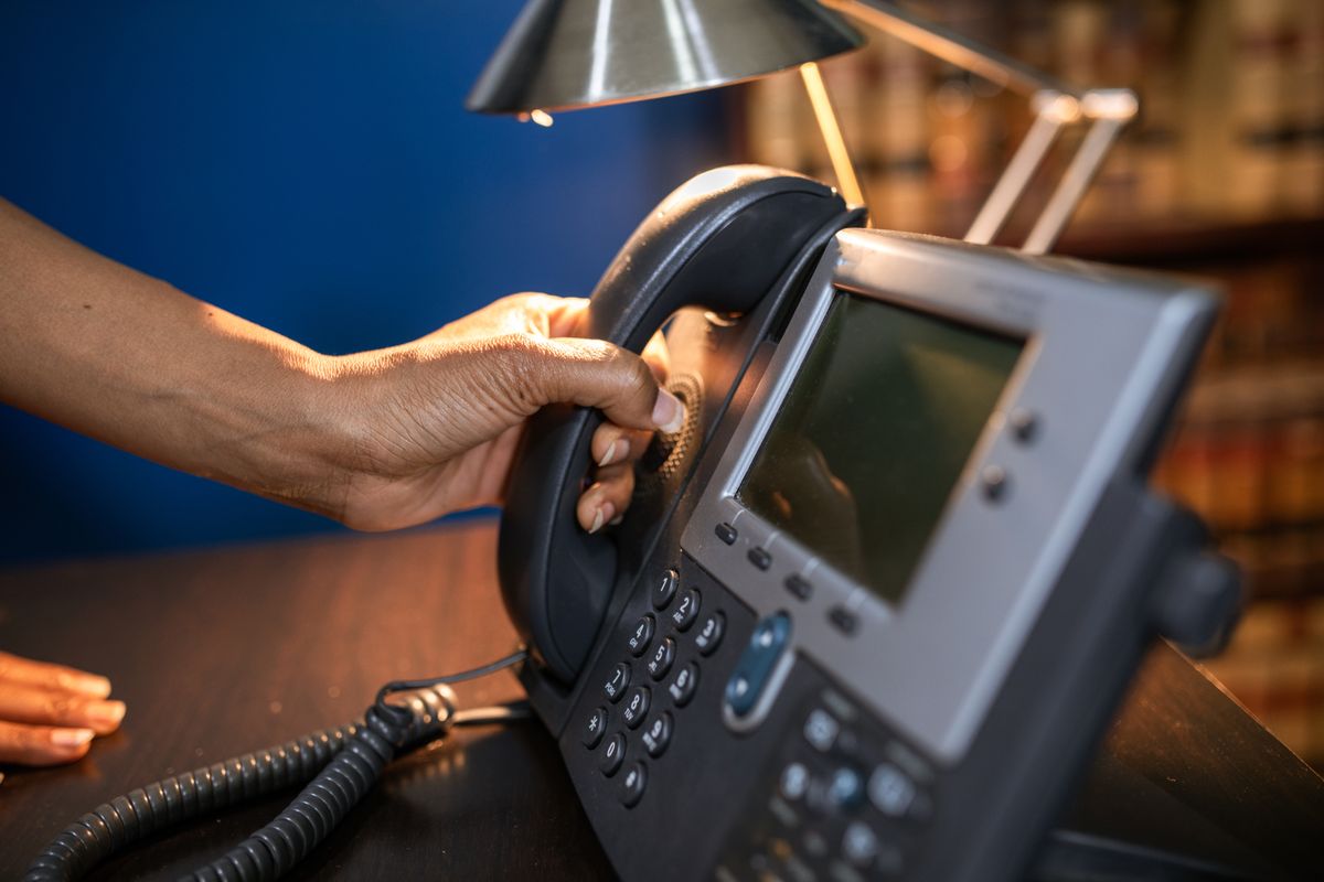 Mão atendendo um telefone IP de mesa em um escritório.